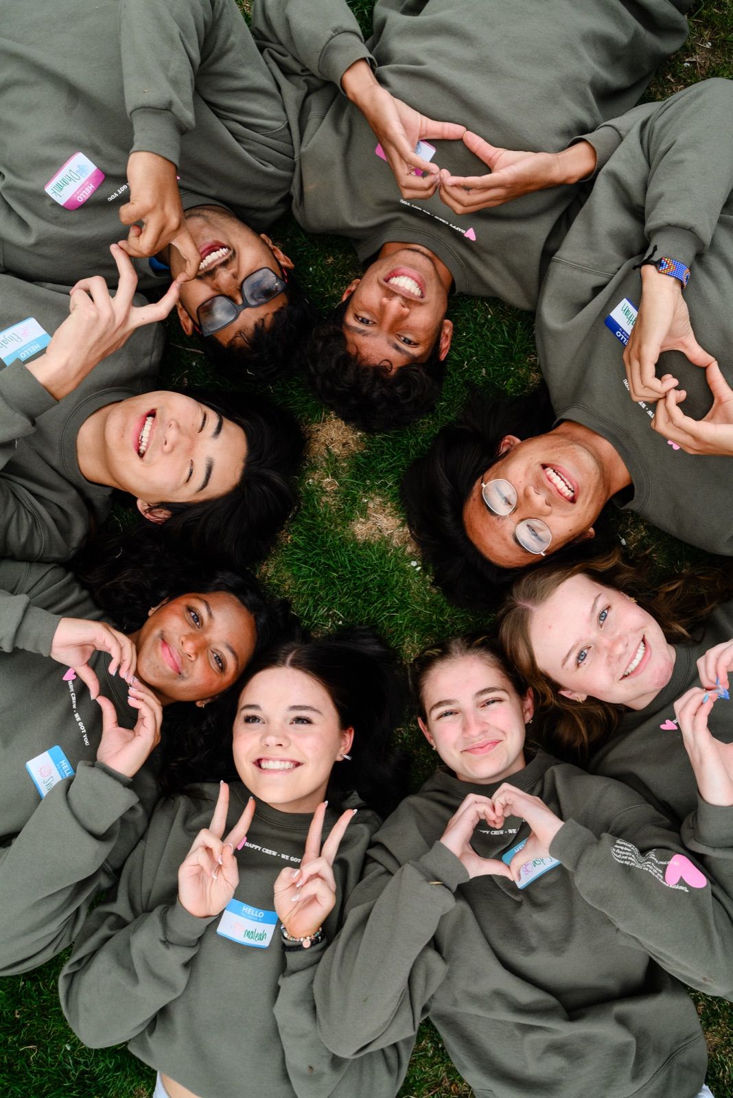 A circle of teens lying on the grass with their heads together, seen from above