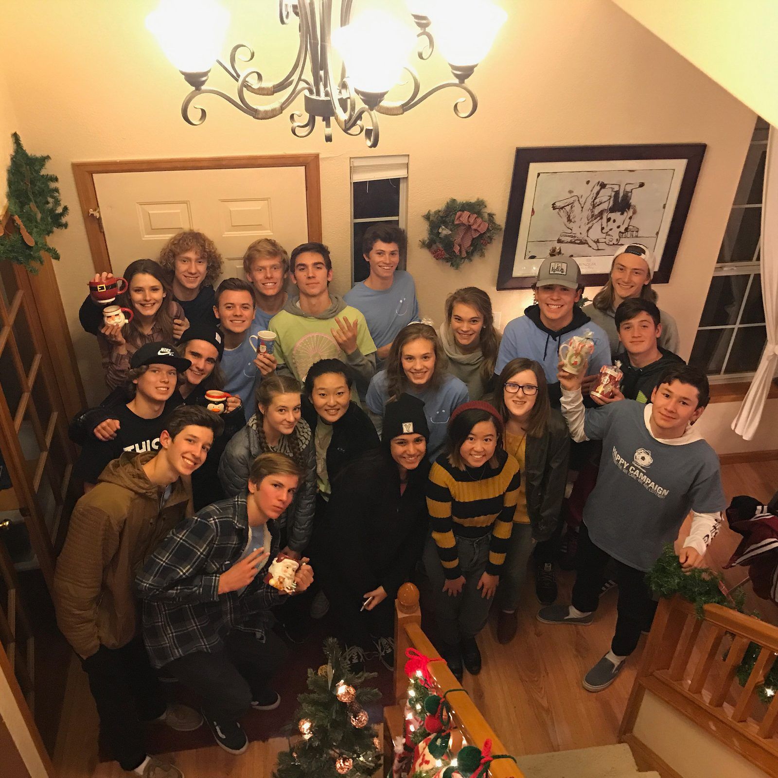 A crowd of teens on a staircase and landing at a Christmas party in a house, smiling up at the camera