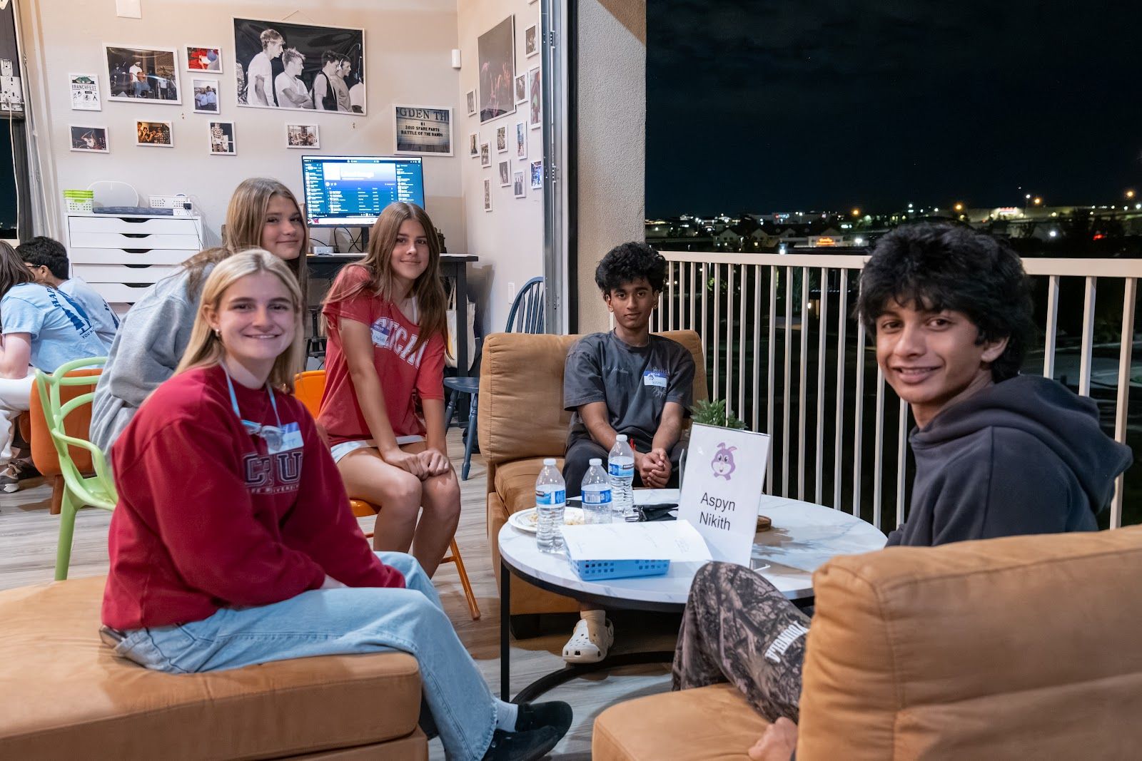 Teens on couches around a low table upstairs, smiling at the camera