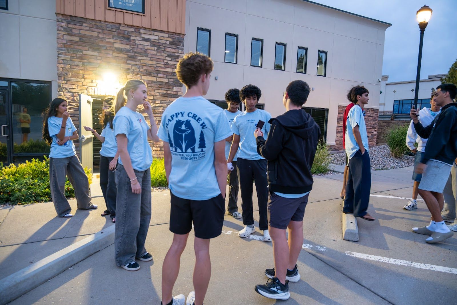 Student leaders in Happy Crew tees outside at dusk, before the doors open
